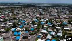 FILE - This June 18, 2018 photo shows an aerial view of the Amelia neighborhood, with many homes still covered in blue tarps, in the municipality of Catano, east of San Juan, Puerto Rico. 