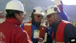 Chile's Minister of Mining Laurence Golborne, left, holds up a bottle of champagne as he speaks to unidentified members of the rescue team after the T-130 drill reached the 33 trapped miners at the San Jose mine near Copiapo, Chile Saturday Oct. 9, 2010.
