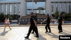 FILE - Policemen patrol as a woman walks past in front of a court, where a trial of suspects of the Kunming railway station attack is taking place, in Kunming, Yunnan province September 12, 2014.