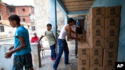Residentes ayudan a descargar y apilar cajas de alimentos básicos, como pasta, azúcar y harina, proporcionados por un programa de asistencia alimentaria del gobierno, en el barrio pobre de Petare, en Caracas, el 30 de abril de 2021.