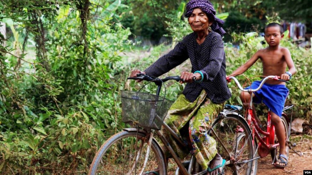 Im Chaem, a former Khmer Rouge cadre, is riding a bike along with her grandson in Anlong Veng, in Oddar Meanchey province in Cambodia, Sunday April 23, 2017. (Sun Narin/VOA Khmer)