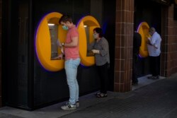 FILE - In this May 5, 2020, file photo, people wearing face masks use cash machines in Caldas de Montbui, near Barcelona, Spain. The coronavirus pandemic has reawakened debate about the continued viability of what has been the physical lifeblood of global economies: paper money and coins. (AP Photo/Emilio Morenatti)