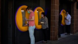 FILE - In this May 5, 2020, file photo, people wearing face masks use cash machines in Caldas de Montbui, near Barcelona, Spain. The coronavirus pandemic has reawakened debate about the continued viability of what has been the physical lifeblood of global economies: paper money and coins. (AP Photo/Emilio Morenatti)