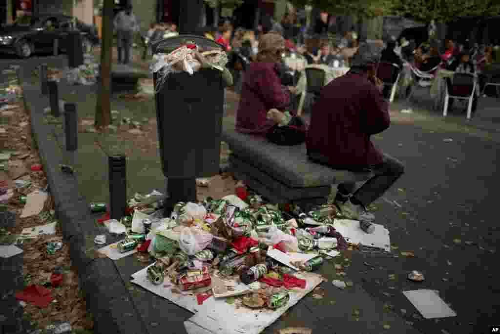 A couple sit on a public bench as garbage spills out of a full trash can during the sixth day of a garbage collectors strike, in Madrid, Spain. Street cleaners and garbage collectors, who work in the city&#39;s public parks, walked off the job in a strike called by trade unions to contest the planned layoff of more than 1,000 workers.