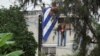 El actor, dramaturgo y líder del proyecto Archipiélago Yunior García, de 39 años, es visto detrás de una ventana de su casa mientras la gente cuelga una bandera cubana en la azotea, en La Habana, Cuba, el 14 de noviembre de 2021. 