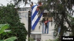 El actor, dramaturgo y líder del proyecto Archipiélago Yunior García, de 39 años, es visto detrás de una ventana de su casa mientras la gente cuelga una bandera cubana en la azotea, en La Habana, Cuba, el 14 de noviembre de 2021. 
