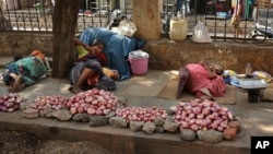 Indian vendors selling onions rest on a sidewalk under the shade of a tree on a hot summer day in Hyderabad, India, Monday, May 25, 2015. 