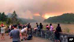 This photo, provided by Inciweb, shows people at a viewpoint overlooking the Columbia River watching the Eagle Creek wildfire burning in the Columbia River Gorge east of Portland, Ore., Sept. 4, 2017. A lengthy stretch of highway Interstate 84 remains closed as crews battle the growing Eagle Creek wildfire that has also caused evacuations and sparked blazes across the Columbia River in Washington state.