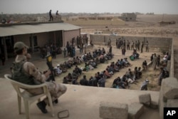 FILE - Displaced people who fled from Islamic State-held territory sit outside a mosque guarded by Iraqi soldiers in Shuwayrah, south of Mosul, Iraq, Nov. 1, 2016.