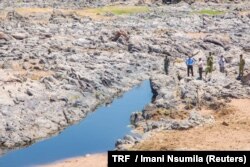 FILE - January Makamba, Tanzanian Minister of State for the Environment, and other officials inspect the dwindling water of the Ruaha river, in Kilolo district, Tanzania, Oct. 19, 2016.