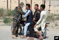 In this July 10, 2018, photo, an Afghan national army soldier searches three men on a motorcycle at a checkpoint on the outskirts of Kabul, Afghanistan.