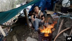 FILE - A man who goes by the name of D cooks lunch from a makeshift tent where he lives in the Jungle, a homeless encampment in San Jose, California, March 4, 2014.