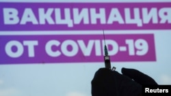 FILE - A health care worker prepares a Sputnik vaccine shot against COVID-19 at a vaccination site at Luzhniki Stadium in Moscow, Russia, July 8, 2021. The sign reads "Vaccination against COVID-19." 