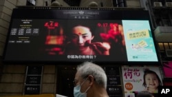 FILE - A man walks past a huge TV screen showing movie listings on a downtown street in Hong Kong, Sept. 17, 2020. Hong Kong censors now have the power to ban films if they determine they endanger national security.