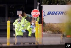 Workers wearing protective masks stand at an entrance to a Boeing production plant to hand out masks to other workers entering Tuesday, April 21, 2020, in Everett, Wash. (AP Photo/Elaine Thompson)