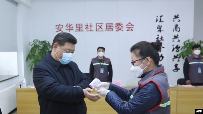 中国国家主席习近平戴着口罩视察北京安华里小区时一名防疫人员检测他的体温。（2020年2月10日）