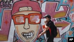 Un hombre usa una máscara facial como medida de precaución contra la propagación del nuevo coronavirus al pasar frente a un mural en el centro de Quito, Ecuador, el domingo 22 de marzo de 2020.
