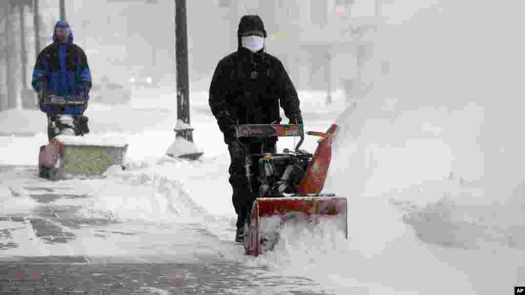 Workers try to clear snow from city sidewalks during a winter snowstorm in Boston, Jan. 27, 2015.