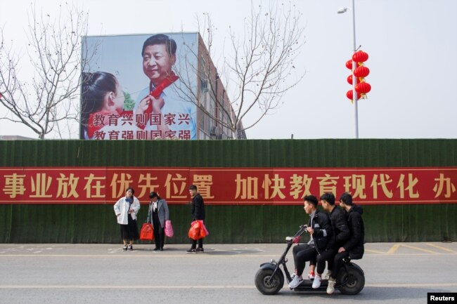 Men ride a scooter past a poster showing Chinese President Xi Jinping on the side of a school building in Henan province, China February 22, 2019.