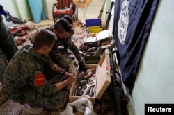 FILE - Fighters of Syrian Democratic Forces inspect weapons and munitions recovered at the former positions of the Islamic State militants inside a building at the frontline in Raqqa, Syria, Oct. 7, 2017.