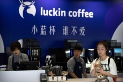 FILE - A customer picks up her order from a Luckin Coffee pop-up shop at the World Robot Conference in Beijing, Aug. 15, 2018.
