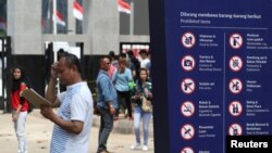 Seorang pria berdiri di samping papan petunjuk barang-barang yang dilarang dibawa di pintu gerbang kompleks olahraga Gelora Bung Karno, menjelang Asian Games 2018 di Jakarta, Indonesia, 17 Agustus 2018. 