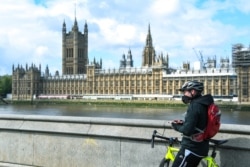 A man, wearing a protective mask, stands with his bike on the south bank of the River Thames against the backdrop of the Houses of Parliament, in London, Britain, May 1, 2020.
