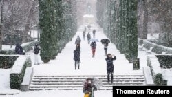 People walk during heavy snowfall in Retiro park in Madrid, January 8, 2021.