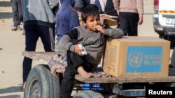 Un niño palestino se sienta junto a una caja de ayuda proporcionada por la UNRWA fuera de un punto de distribución, en medio de un alto el fuego entre Israel y Hamás, en Khan Younis, en el sur de la Franja de Gaza, el 4 de febrero de 2025.