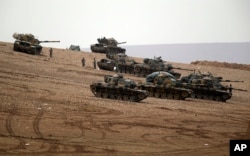 FILE - Turkish soldiers hold their positions with their tanks on a hilltop on the outskirts of Suruc, at the Turkey-Syria border, overlooking Kobani, Syria, during fighting between Syrian Kurds and Islamic State militants, Oct. 12, 2014.