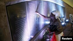 Margaret Achieng Jow, who's daughter Doreen was killed in the 1998 U.S. Embassy in Nairobi bombing, holds a cross on a wall displaying the names of people killed during the attack at a ceremony marking the 20th anniversary of the bombing at the August 7th