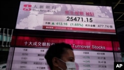 A woman wearing a face mask walks past a bank's electronic board showing the Hong Kong share index at Hong Kong Stock Exchange Tuesday, July 21, 2020. Asian shares were mostly higher Tuesday as hopes rose about a vaccine being developed to fight the…