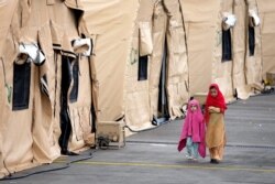 Two kids walk next to tents at the Ramstein U.S. Air Base in Ramstein, Germany, Aug. 30, 2021. The largest American military community overseas houses thousands Afghan evacuees in a tent city at the airbase.
