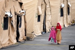Two kids walk next to tents at the Ramstein U.S. Air Base in Ramstein, Germany, Aug. 30, 2021. The largest American military community overseas houses thousands Afghan evacuees in a tent city at the airbase.