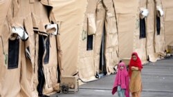 Two kids walk next to tents at the Ramstein U.S. Air Base in Ramstein, Germany, Monday, Aug. 30, 2021. The largest American military community overseas houses thousands Afghan evacuees in a tent city at the airbase. (AP Photo/Matthias Schrader)