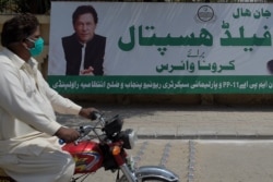 FILE - A man wearing face mask rides his motorbike past a billboard showing a picture of Prime Minister Imran Khan along with a government advisory on coronavirus restrictions, in Rawalpindi, Pakistan, April 15, 2020.