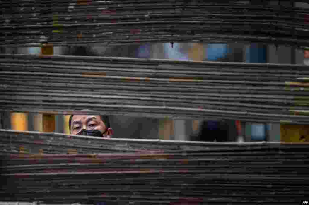 A man wearing a face mask looks through a barrier in a neighborhood in Wuhan, the central Chinese city where the coronavirus first emerged last year, in central Hubei province. 