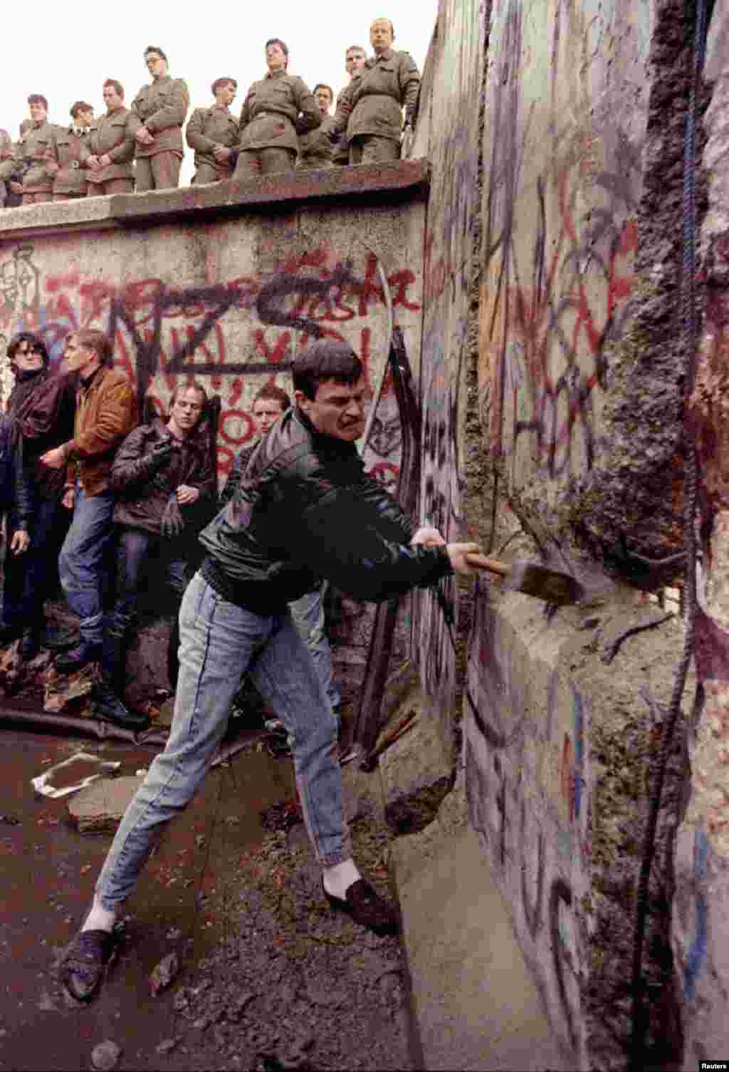 A demonstrator pounds away at the Berlin Wall as East German border guards look on from above at the Brandenburg Gate 11 November 1989.WR - RTRRSTV