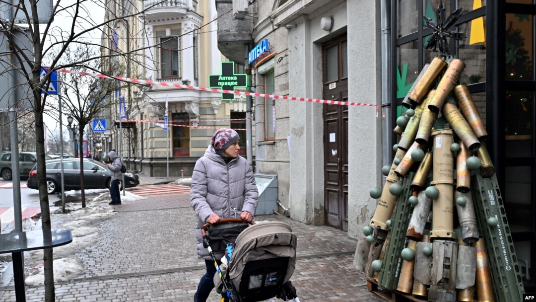 Žena gura kolica dok prolazi pored simboličnog božićnog drvca napravljenog od istrošenih čaura i druge istrošene municije podignute ispred kafića u centru Kijeva 18. decembra 2023. (Photo by Sergei SUPINSKY / AFP)