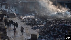 Palestinians walk past a pile of burning garbage in Gaza City, Feb. 12, 2025. 