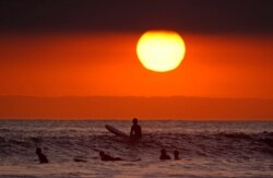 FILE - Surfers wait for waves as the sun goes down the day before the beach was scheduled to close during the coronavirus outbreak, April 30, 2020, in Newport Beach, Calif.