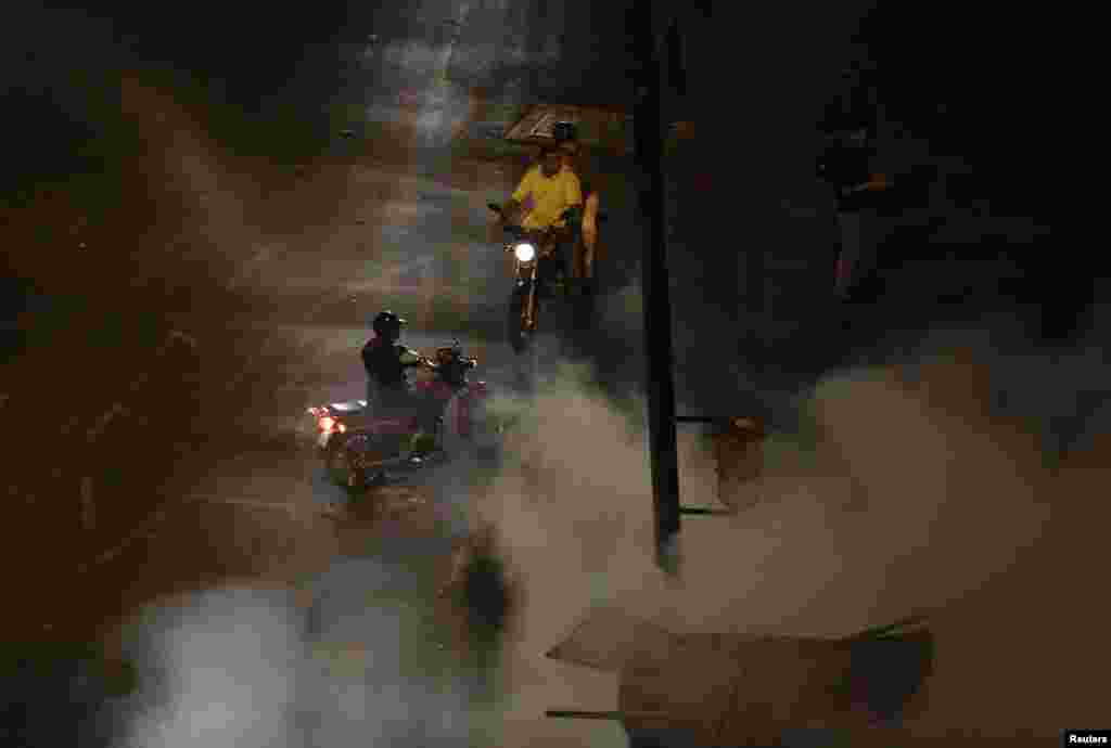 Motociclistas observam os bombeiros a tentar apagar as chamas da motorizadas incendiadas pelos manifestantes anti-governo na Praça de Altamira em Caracas, Fev. 26, 2014.&nbsp;