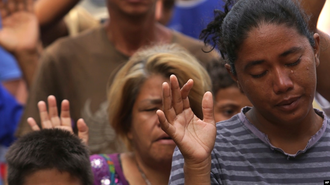 In this March 11, 2018 photo, a tear runs down the cheek of Venezuelan woman praying during religious service in Simon Bolivar Square where many are living in tents in Boa Vista, Roraima state, Brazil. 