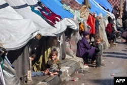 A woman and children sit outside tents sheltering displaced Palestinians in Rafah in the southern Gaza Strip on February 8, 2024, amid the ongoing conflict between Israel and the Palestinian militant group Hamas. (Photo by Mohammed ABED / AFP)