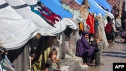 A woman and children sit outside tents sheltering displaced Palestinians in Rafah in the southern Gaza Strip on Feb. 8, 2024.