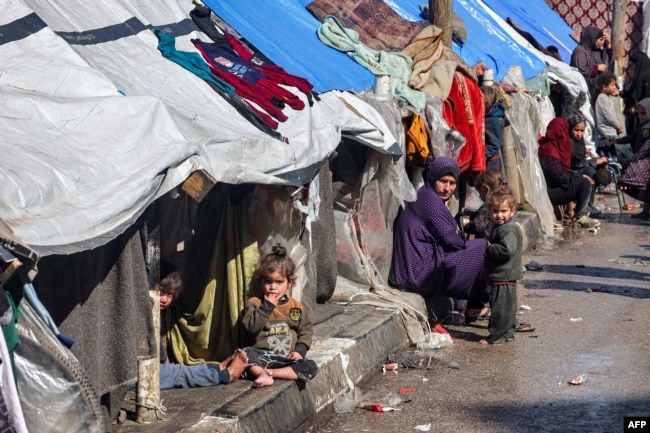 A woman and children sit outside tents sheltering displaced Palestinians in Rafah in the southern Gaza Strip on February 8, 2024, amid the ongoing conflict between Israel and the Palestinian militant group Hamas. (Photo by Mohammed ABED / AFP)