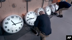 Clockmakers Rich Finn, left, and Tom Erb adjust the time zone controllers on a series of clocks at the Electric Time Company in Medfield, Massachusetts, Oct. 30, 2024.