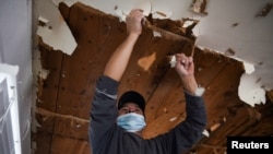 FILE - A contractor removes material from a ceiling in a recently purchased home that sustained water damage because of broken pipes, which froze during an unprecedented winter storm, in Houston, Texas, Feb, 19, 2021.