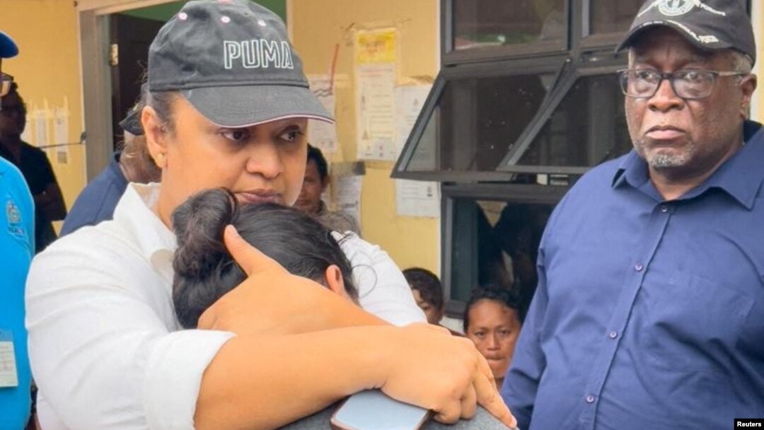 La ministra de Educación de Guyana, Priya Manickchand, consuela a uno de los padres de uno de varios niños que murieron en el incendio de un dormitorio de una escuela secundaria, en Mahdia, Guyana, mientras el primer ministro Mark Phillips observa.