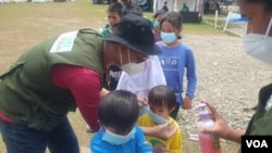 Relawan dari IBU Foundation memasangkan masker wajah pada salah seorang anak di shelter Terintegrasi di Stadion Manakarra, Mamuju, Sulawesi Barat, Minggu, 31 Januari 2021. (Foto: Yoanes Litha/VOA)